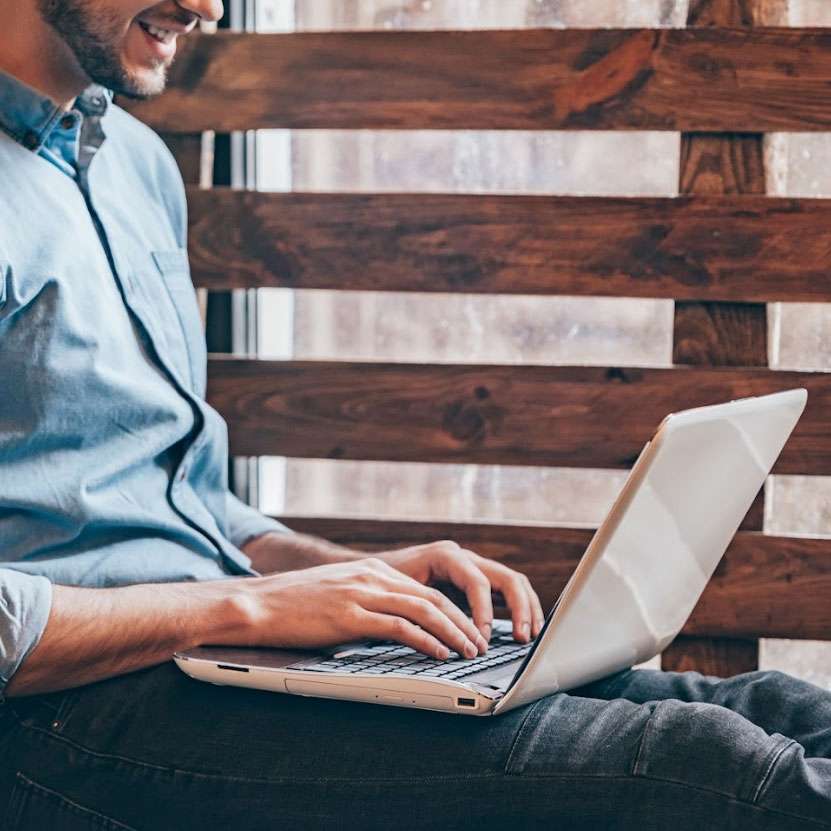 Person typing on a laptop, sitting against a wooden backdrop, illustrating digital marketing and blogging strategies for enhancing SEO.