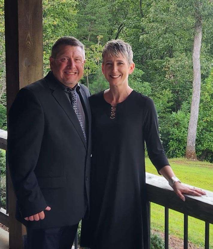 Richard and Wendy Burnham, founders of The Salt Net, standing together on a porch with a lush green background, showcasing their professional partnership in innovative marketing solutions.
