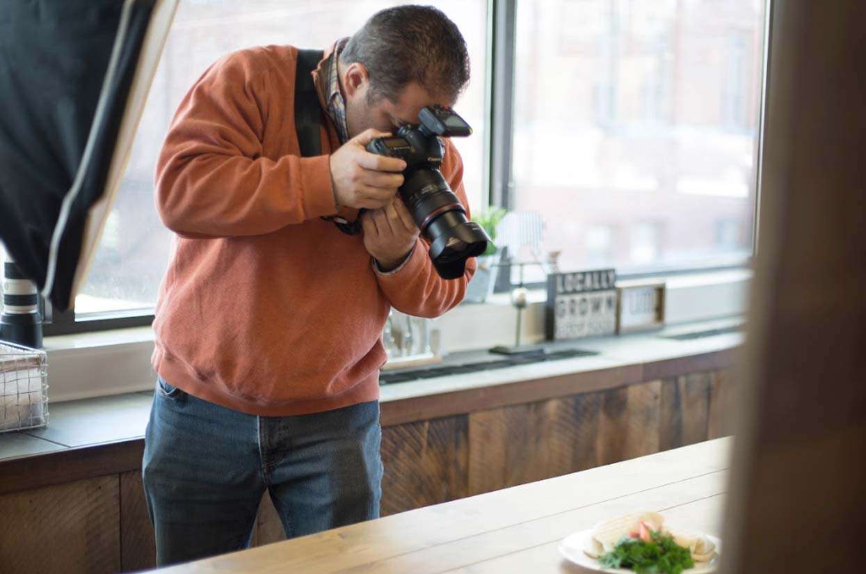 Person photographing a plate of food with a camera in a well-lit indoor setting, emphasizing visual content creation for engaging blog posts.