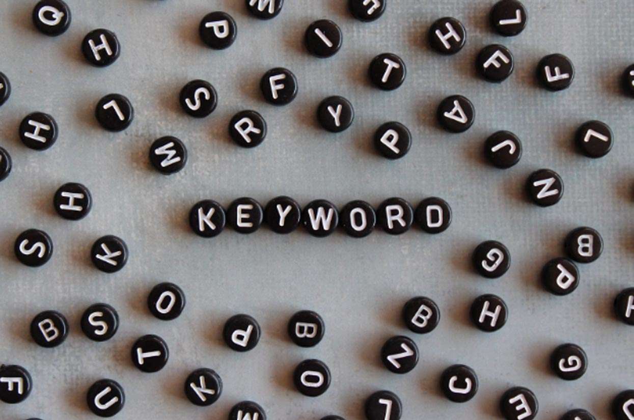 Black circular letter tiles scattered on a surface, prominently featuring the word "KEYWORD" in the center, symbolizing digital marketing and SEO strategies.
